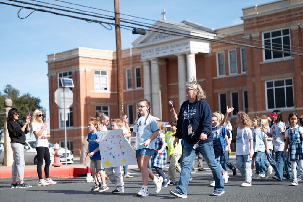 Students (left) Beau Burg, Gage Thompson and Cricket Frantzen lead their class in the parade along with their teacher Jeretta West. The parade traveled down West San Antonio Street, directly in front of the historic school building at the corner of South Orange Street.